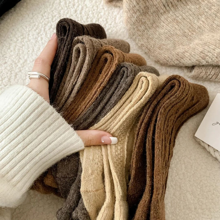 Frau hält gestrickte Wollsocken in Erdtönen, gemütlich, warm, modisch, Herbst-Winter-Accessoire.