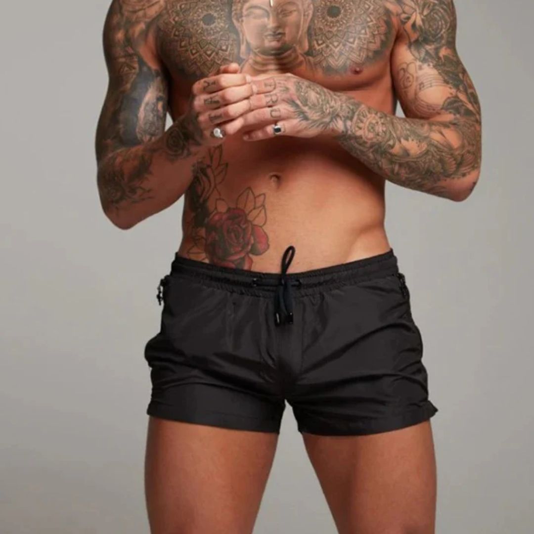 Mann mit Tattoos trägt schwarze Badehose, muskulöser Oberkörper, Mode, Fitness, Strandbekleidung.