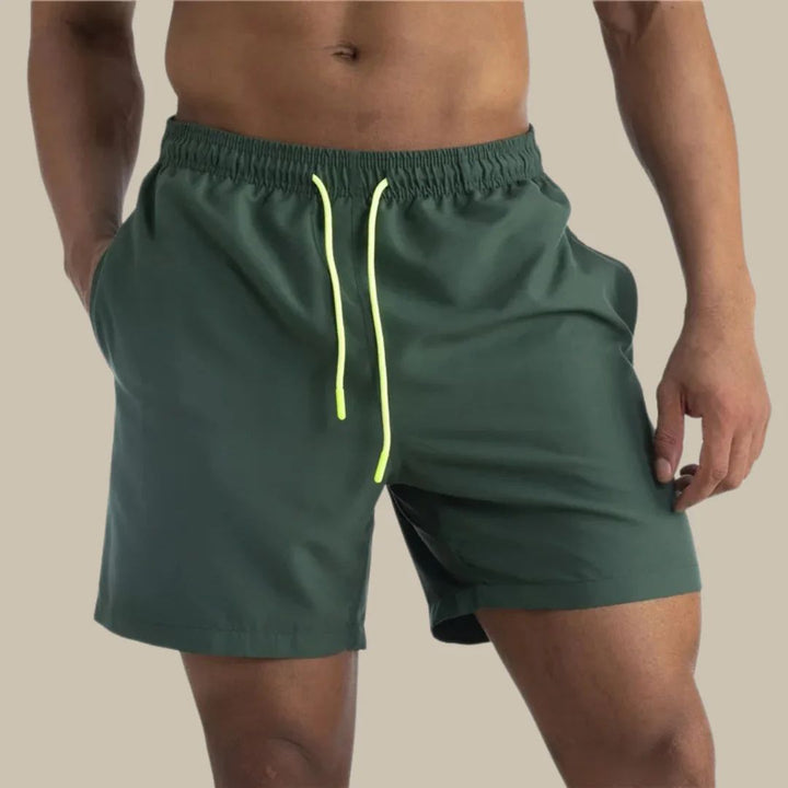 Mann in grüner Badehose mit gelbem Kordelzug, sportlich, Strandmode, Herrenbekleidung.