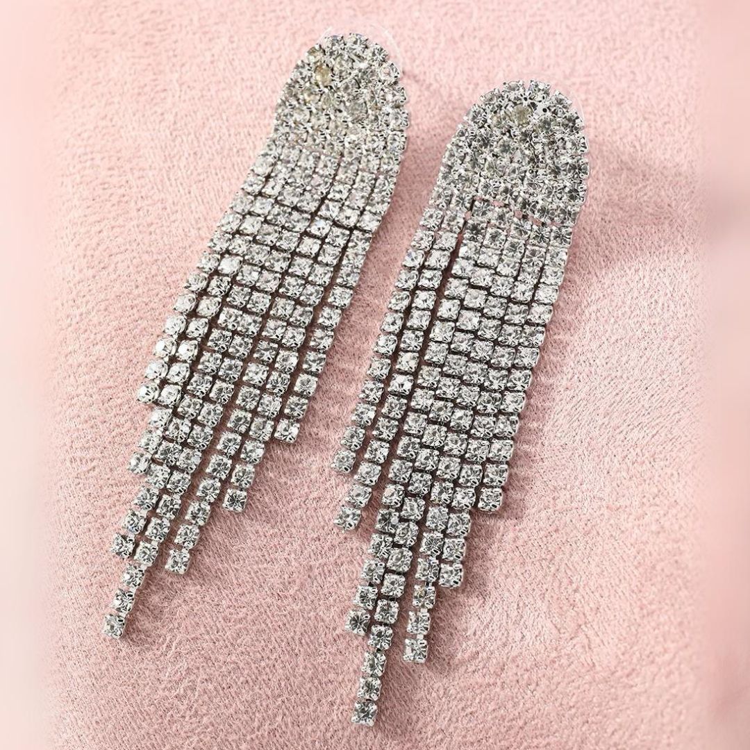 Silberne Strass-Ohrringe mit langen Fransen auf rosa Hintergrund, glamouröser Schmuck.
