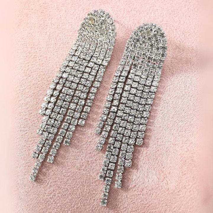 Silberne Strass-Ohrringe mit langen Fransen auf rosa Hintergrund, glamouröser Schmuck.