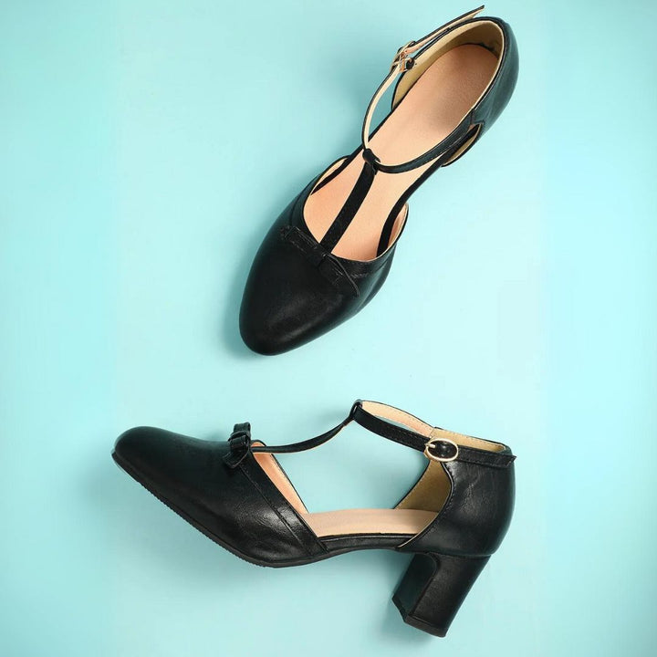 Schwarze Damen-Tanzschuhe mit T-Riemen und Blockabsatz auf hellblauem Hintergrund.