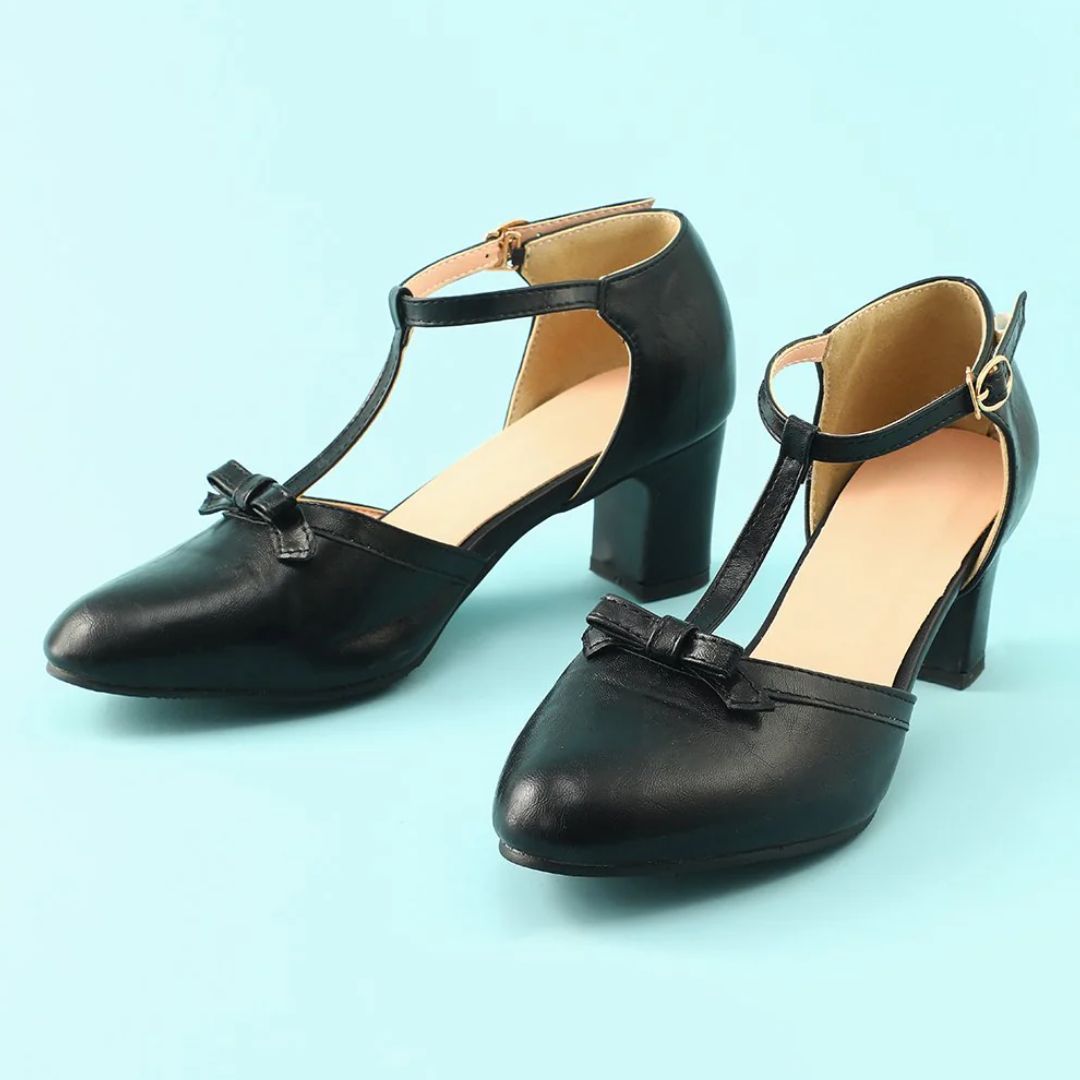 Schwarze Damen-T-Riemen-Pumps mit Blockabsatz und Schleife auf blauem Hintergrund.