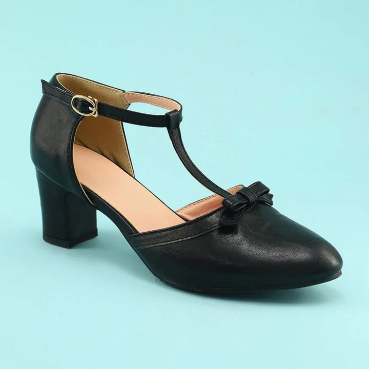 Schwarzer Damenpumps mit T-Riemen, Blockabsatz und Schleife, elegantes Design.