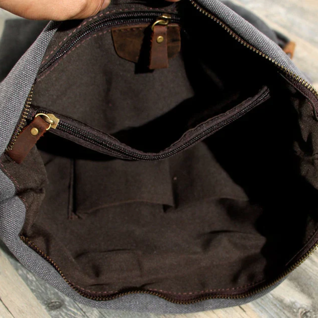 Graue Canvas-Umhängetasche mit braunem Innenfutter und Reißverschlusstasche, ideal für Reisen.