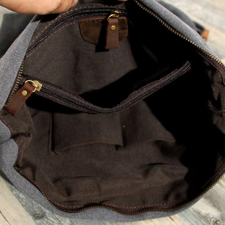 Graue Canvas-Umhängetasche mit braunem Innenfutter und Reißverschlusstasche, ideal für Reisen.