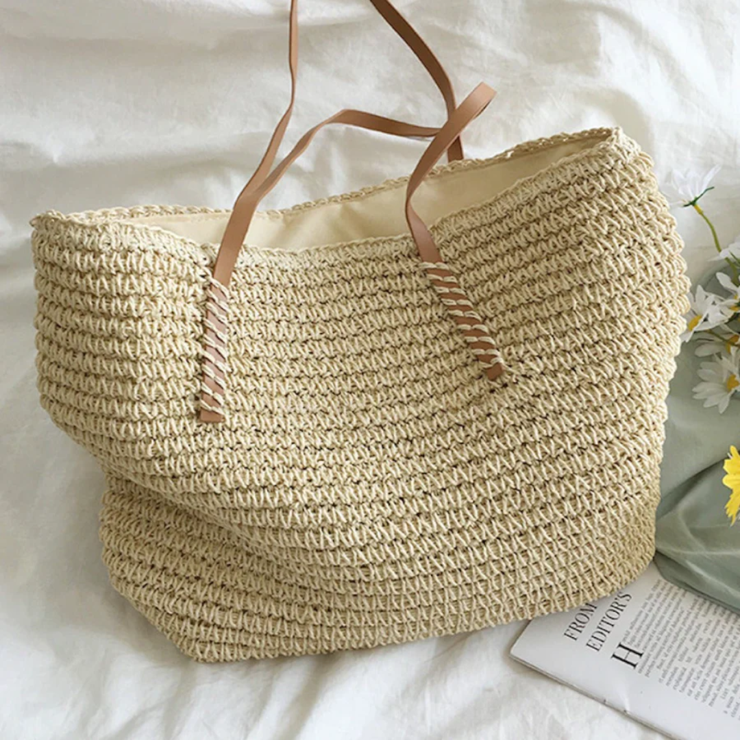 Beiger Strohtasche mit braunen Ledergriffen auf weißem Hintergrund, ideal für Sommer und Strand.