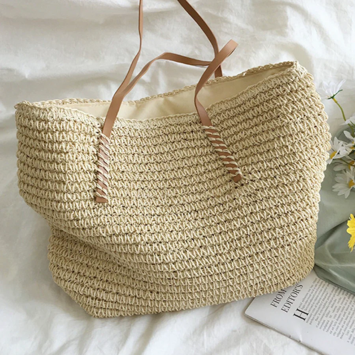Beiger Strohtasche mit braunen Ledergriffen auf weißem Hintergrund, ideal für Sommer und Strand.