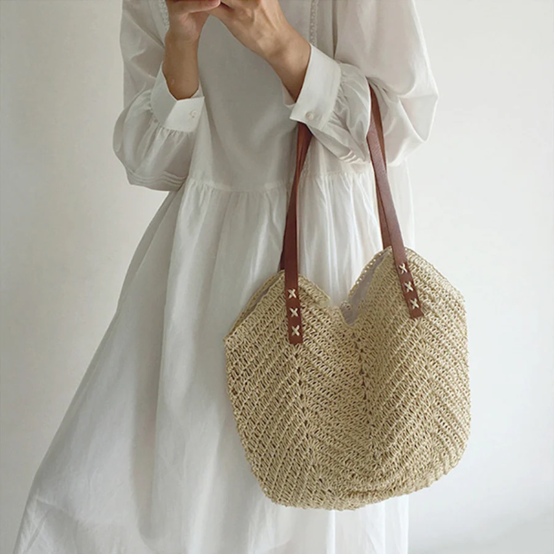 Frau mit weißem Kleid und Strohtasche, braune Ledergriffe, Sommermode, Boho-Stil.