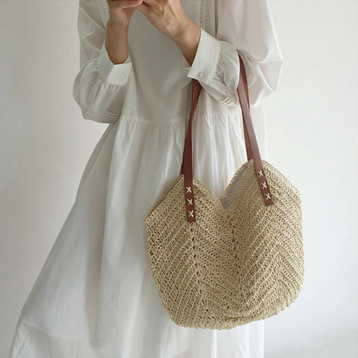 Frau mit weißem Kleid und Strohtasche, braune Ledergriffe, Sommermode, Boho-Stil.