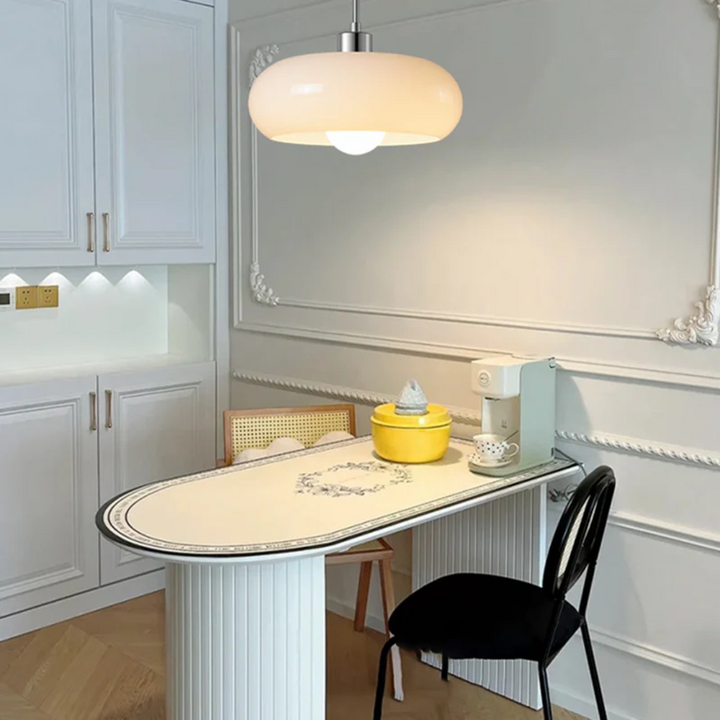 Moderne Küche mit weißem Tisch, gelber Schüssel, schwarzem Stuhl und eleganter Hängelampe.