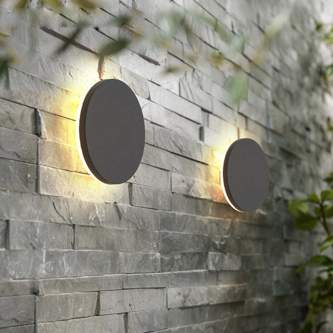 Moderne runde LED-Wandleuchten auf grauer Steinwand im Außenbereich, energiesparend.