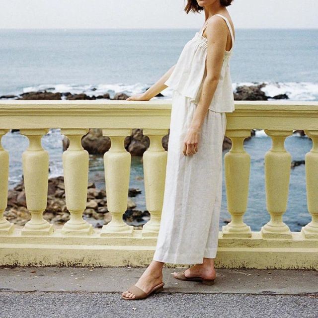 Frau in weißem Sommerkleid am Meer, stehend an einer Balustrade, entspannte Urlaubsstimmung.