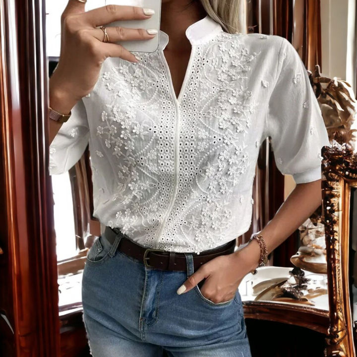 Frau in weißer, bestickter Bluse und blauer Jeans, Spiegel-Selfie, modisch, elegant.
