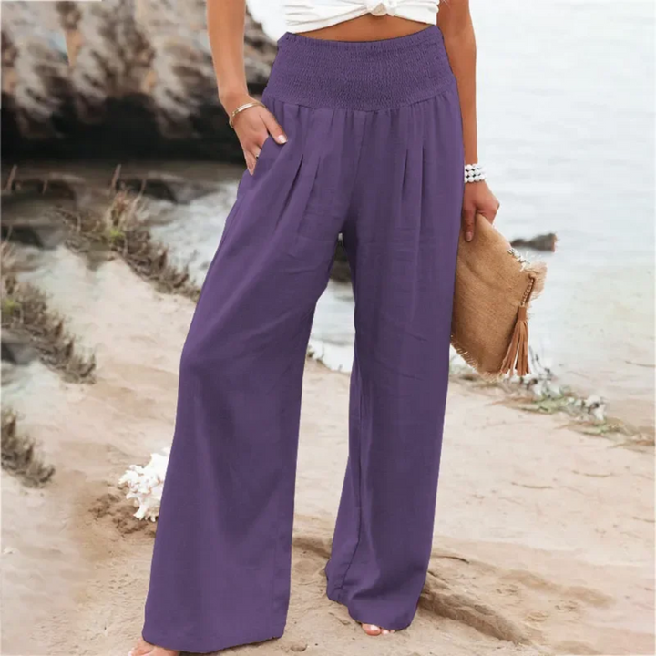 Frau in lila Leinenhose am Strand, Sommermode, weite Passform, lässiger Stil.