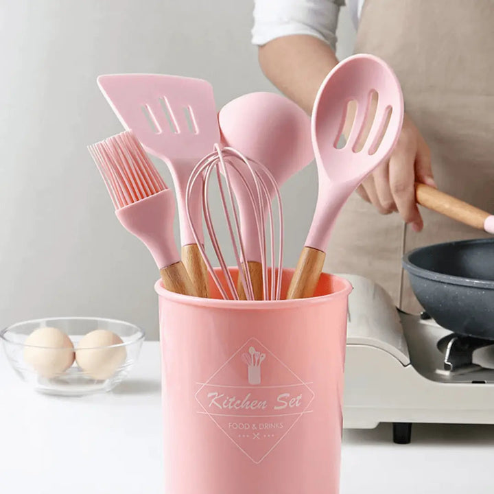 Rosa Silikon-Küchenutensilien-Set mit Holzgriffen in einem rosa Behälter.