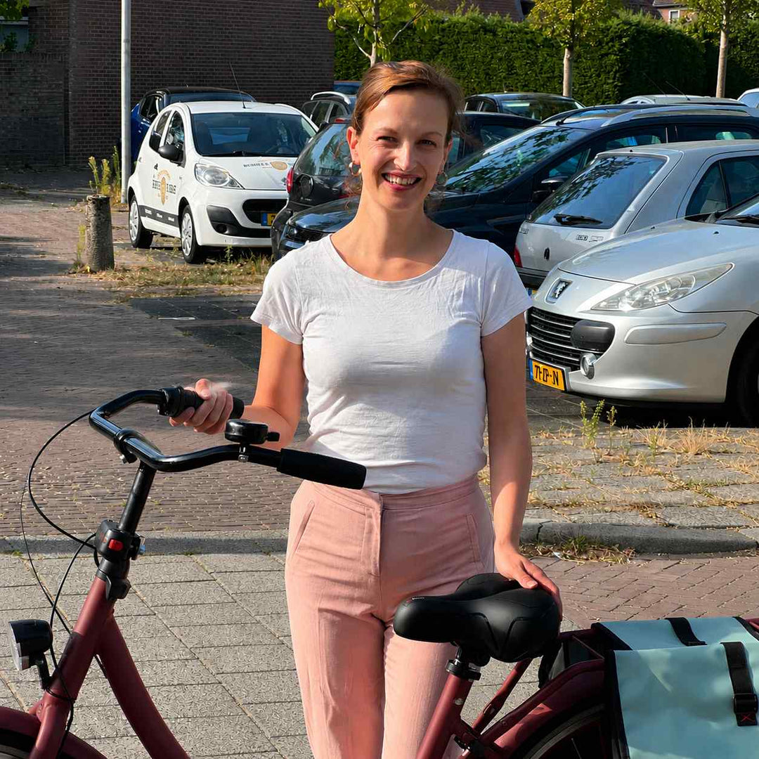 Usměvavá žena stojí na ulici u červeného městského kola, jednou rukou se opírá o černé sedlo, vzadu brašna. 7