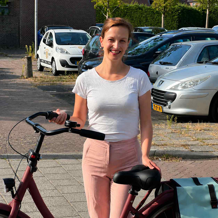 Usměvavá žena stojí na ulici u červeného městského kola, jednou rukou se opírá o černé sedlo, vzadu brašna. 7