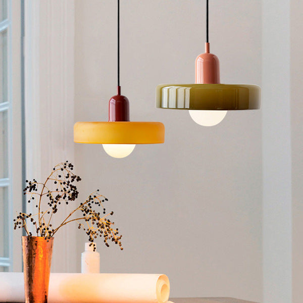 Zwei moderne Hängelampen, gelb und grün, aus Glas über einem Tisch mit Dekoration.