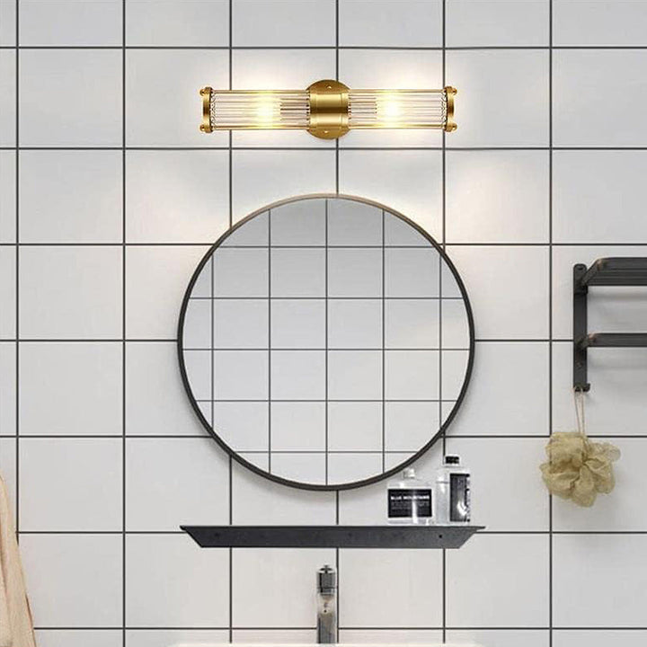 Goldene Wandleuchte über rundem Spiegel im modernen Badezimmer mit Fliesenwand.