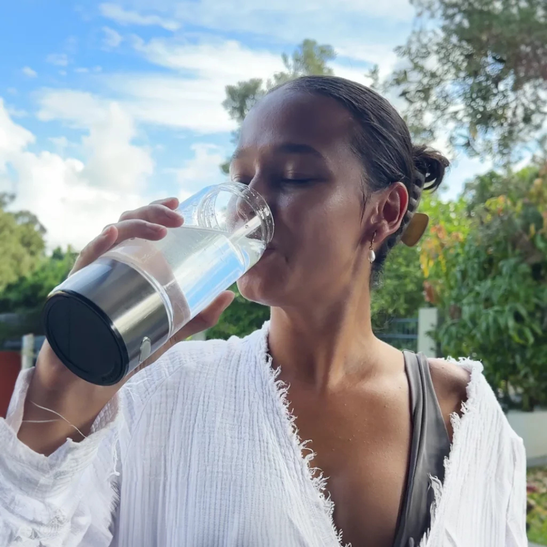 Frau trinkt aus Wasserstoff-Generatorflasche, Glasflasche, Outdoor, gesundheitsbewusst.