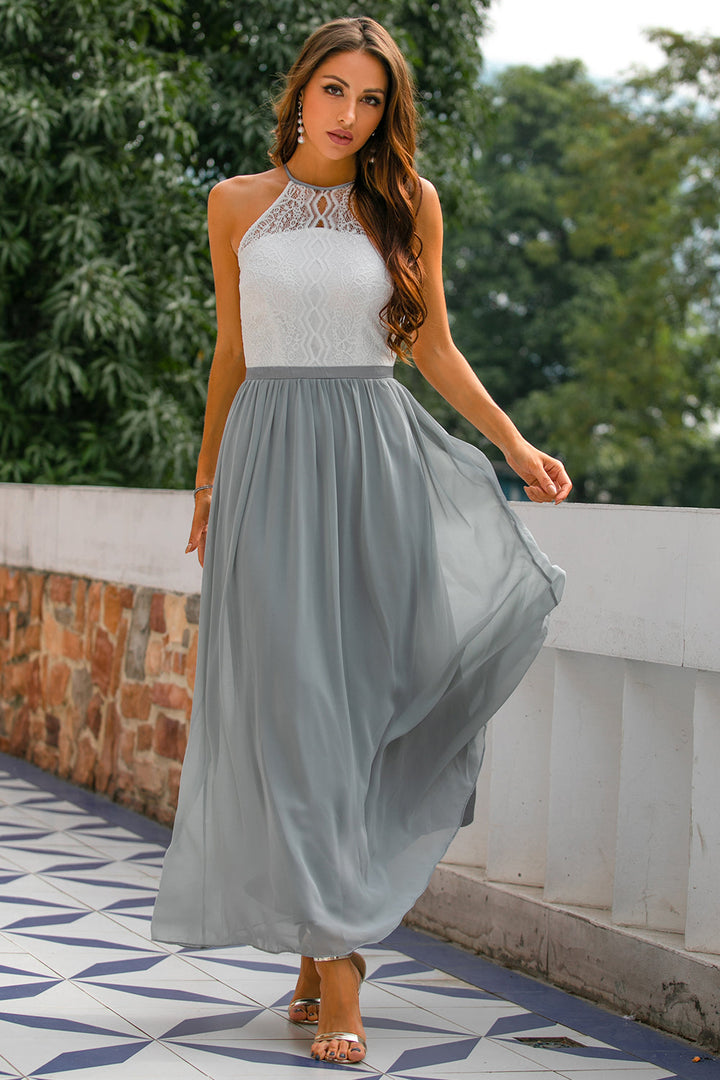 Frau im eleganten, ärmellosen Maxikleid aus Spitze und Chiffon in Weiß und Grau, draußen stehend.