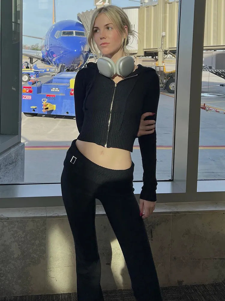 Frau in schwarzem Outfit mit Kopfhörern am Flughafen, Flugzeug im Hintergrund.