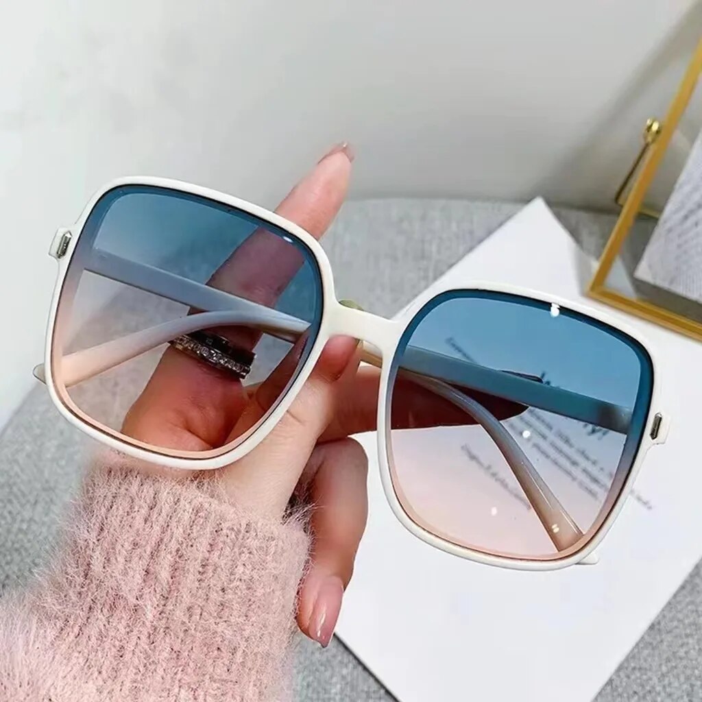 Weiße quadratische Sonnenbrille mit blauen Gläsern, modisches Accessoire auf grauem Hintergrund.