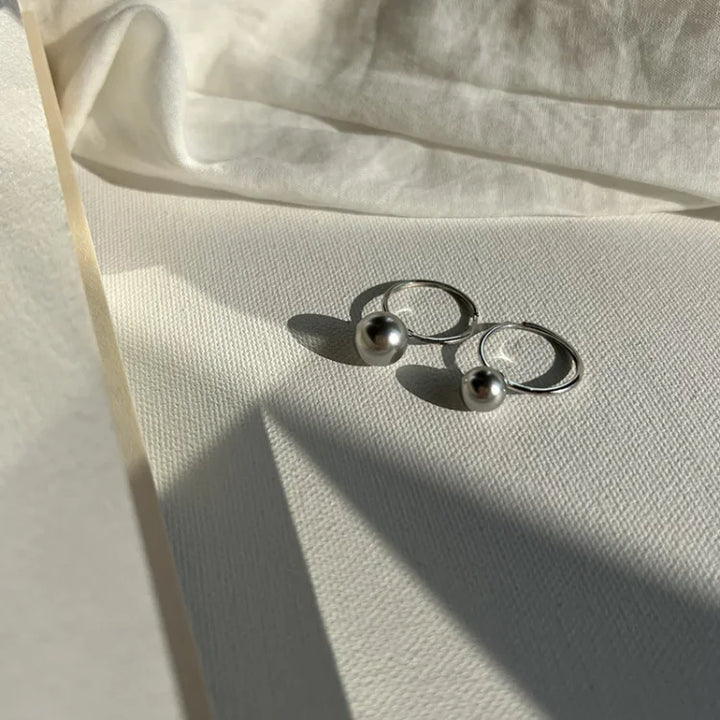 Silberne Ohrringe mit Perlen auf weißem Stoff, eleganter Schmuck, minimalistisches Design.
