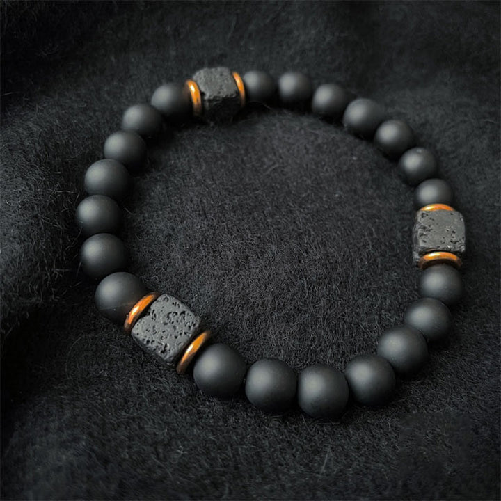 Schwarzes Lavastein-Armband mit matten Perlen, elastisch, auf schwarzem Stoffhintergrund.