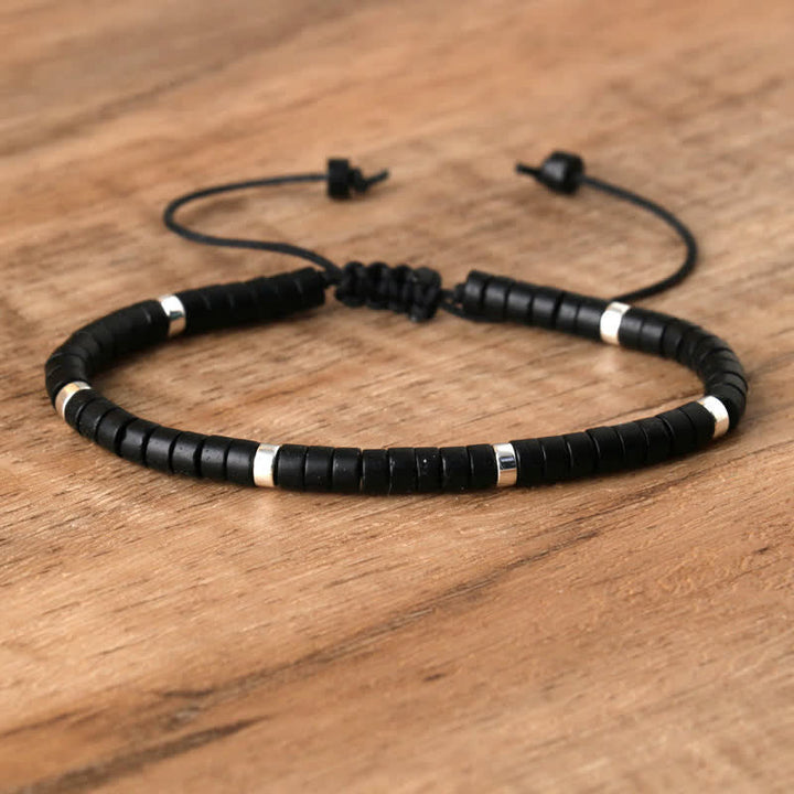 Schwarzes Armband aus Leder mit silbernen Akzenten auf Holzoberfläche, verstellbar.