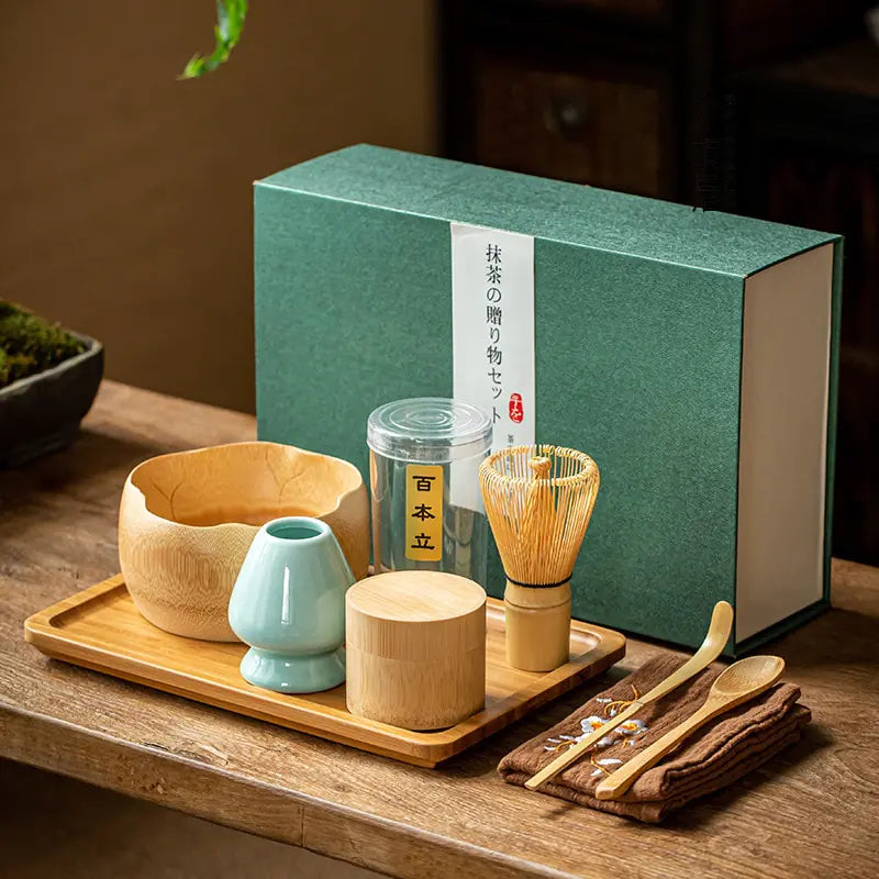 Matcha-Set mit Bambusschale, Besen, Löffel und grünem Geschenkkarton auf Holztisch.