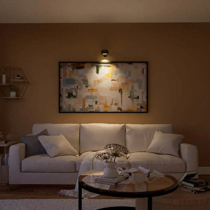 Moderne Wohnzimmer mit beigem Sofa, abstraktem Gemälde und stilvoller Beleuchtung.