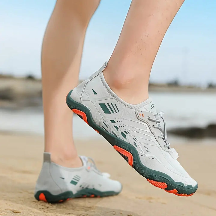 Weiße Outdoor-Sportschuhe mit grünen und orangefarbenen Akzenten am Strand.