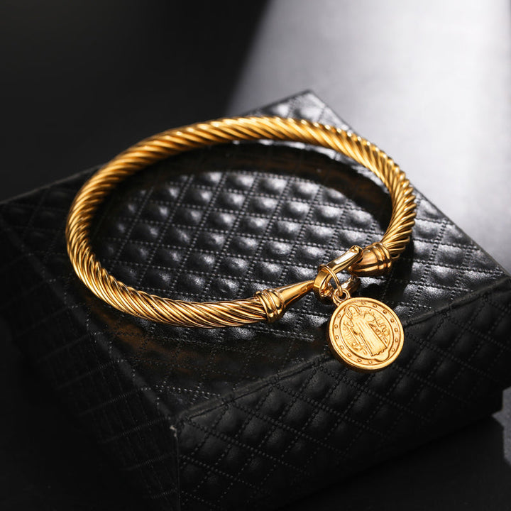 Goldenes Armband mit Anhänger, gedrehtes Design, auf schwarzem Hintergrund, Schmuckaccessoire.