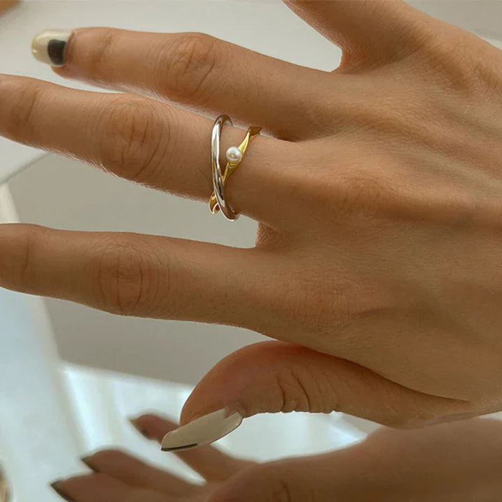 Damenhand mit silbernem und goldenem Ring, Perle, eleganter Schmuck, Nahaufnahme.