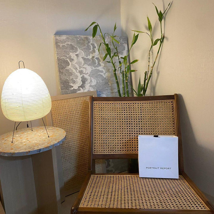 Akari Tischlampe 45 auf Marmortisch, Rattan-Stuhl, Bambuspflanze, modernes Wohnzimmerdekor.