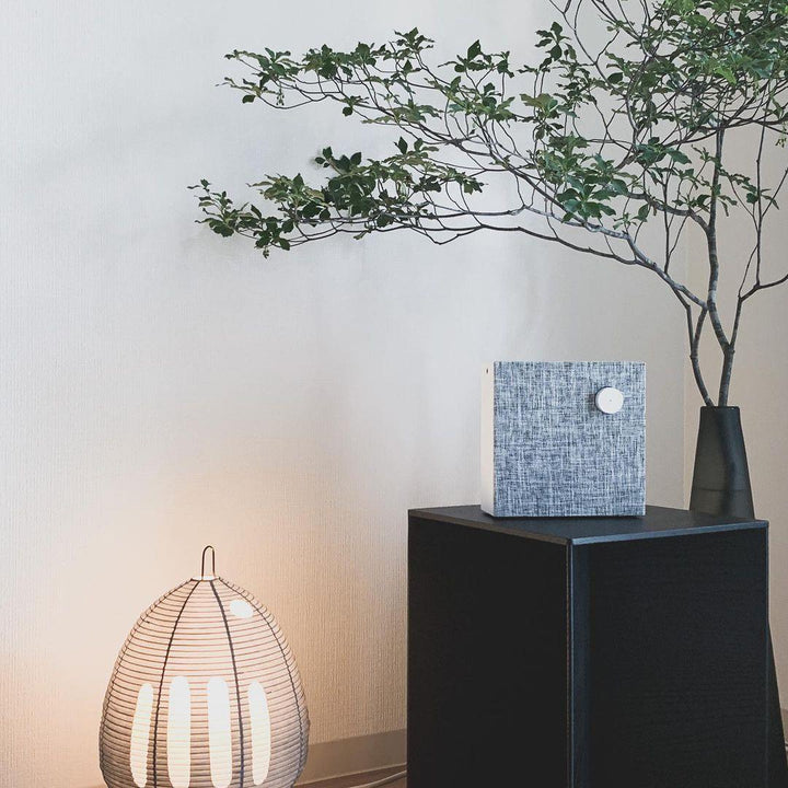 Akari Tischlampe, Papier, Holz, beleuchtet, neben schwarzem Podest mit Pflanze, modernes Design.
