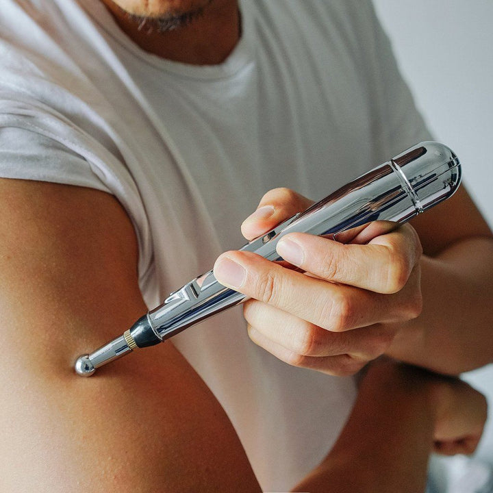 Mann benutzt silbernen Akupunkturstift auf Arm, tragbares Massagegerät, Schmerzlinderung.