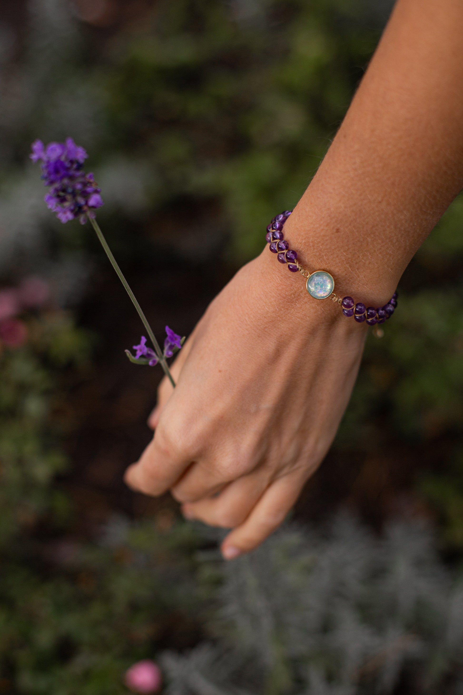 Hand mit lila Armband und Lavendelblüte, Schmuck, Edelstein, Natur, Modeaccessoire.