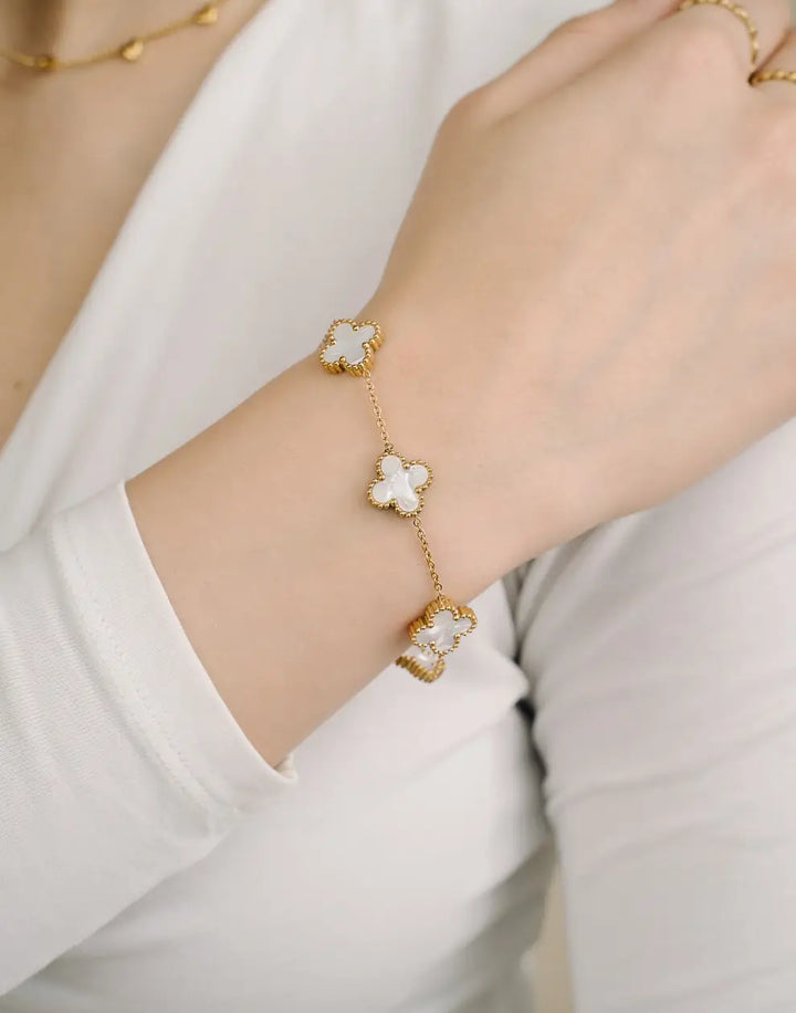 Goldenes Armband mit weißen Kleeblatt-Anhängern, Damenmode, eleganter Schmuck, Nahaufnahme.