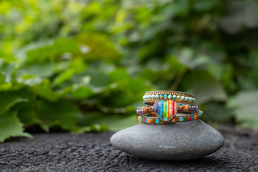 Bunte Perlenarmbänder auf grauem Stein vor grünem Hintergrund, handgefertigter Schmuck.