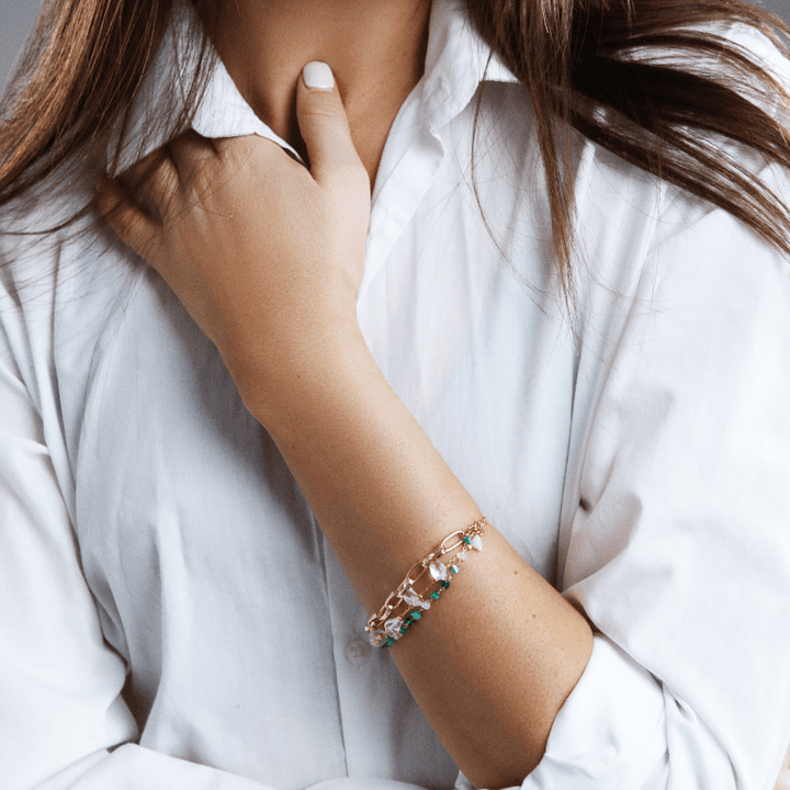 Frau mit weißem Hemd trägt goldfarbenes Armband mit bunten Steinen, modisches Accessoire.