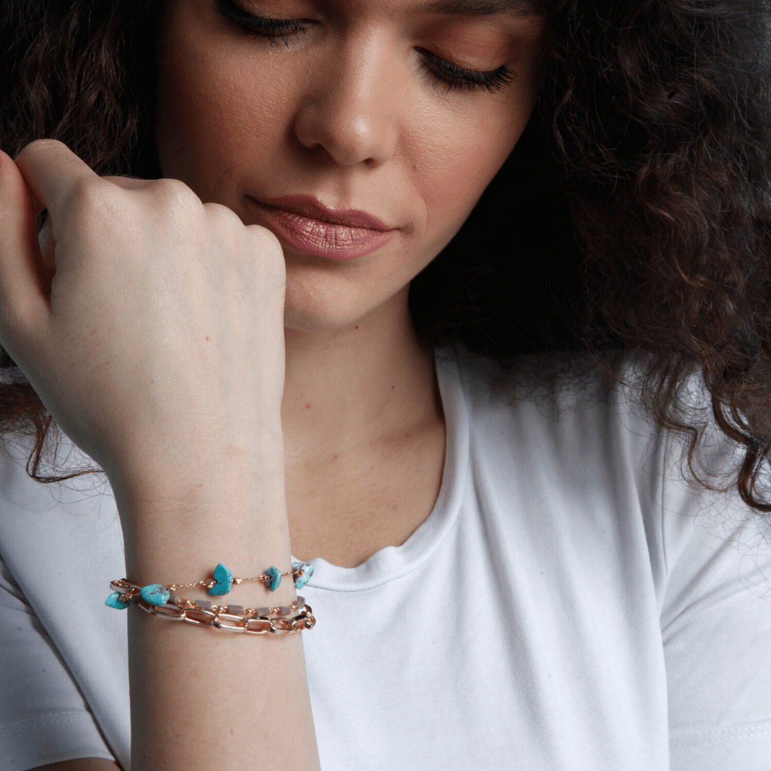 Frau mit goldener Armbandkette und türkisfarbenen Steinen, modisches Schmuckdesign.