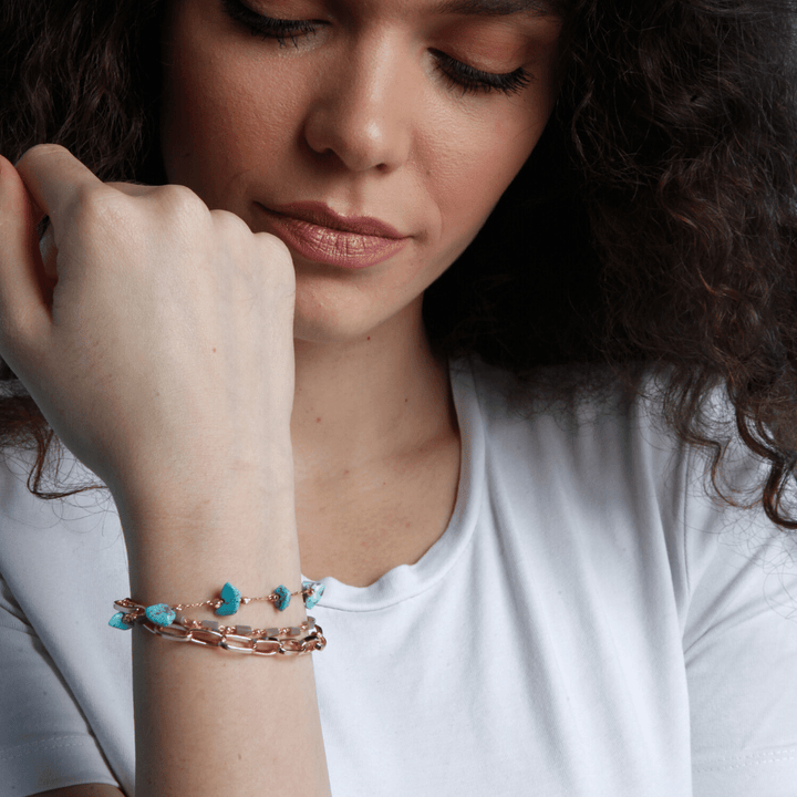 Frau mit goldener Armbandkette und türkisfarbenen Steinen, modisches Schmuckdesign.