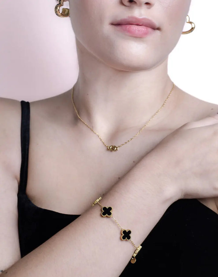 Frau mit schwarzem Kleeblatt-Armband und passender Halskette aus Gold, eleganter Schmuck.