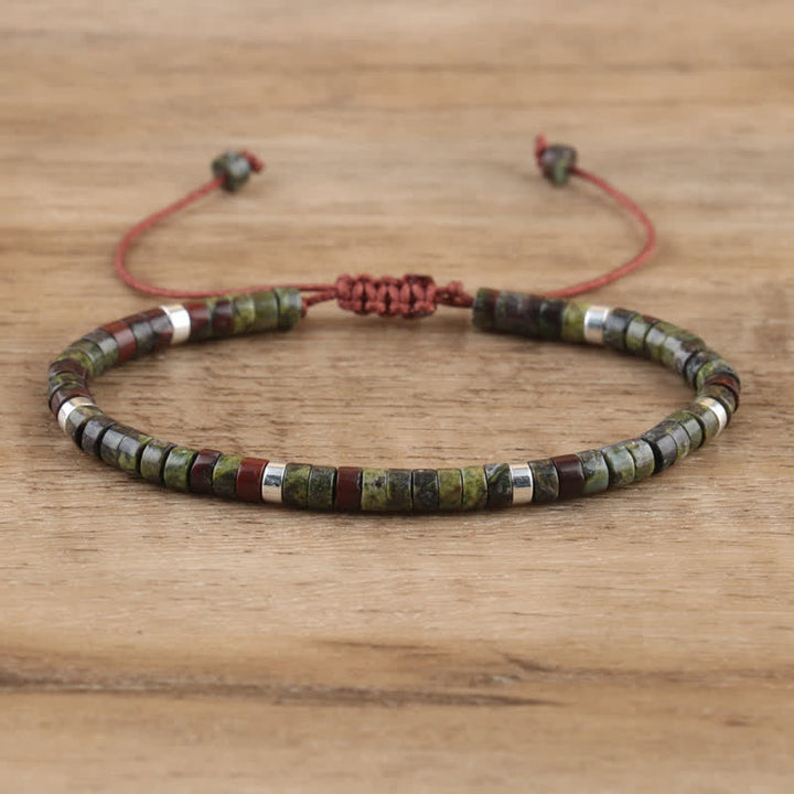 Armband aus grünen und braunen Steinen, verstellbar, handgefertigt, auf Holzoberfläche.
