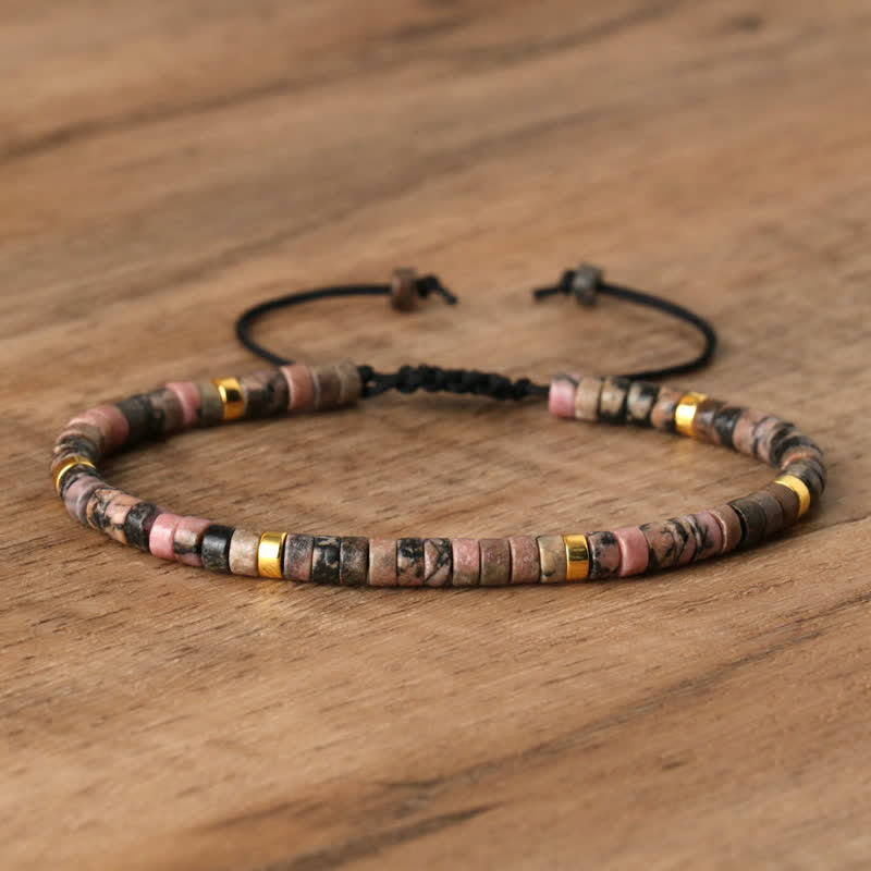 Armband aus Natursteinperlen, rosa und gold, verstellbar, handgefertigt, auf Holzoberfläche.