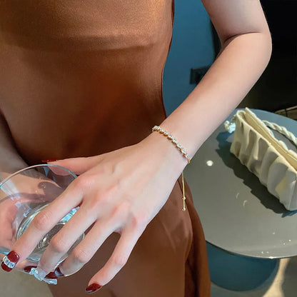 Frau in braunem Kleid mit Perlenarmband hält Glas, elegante Modeaccessoires.