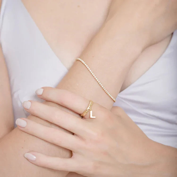 Frau mit goldener Buchstabenring und zartem Armband, Schmuck, Modeaccessoire, elegantes Design.